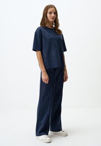Navyblauwe, loszittende top met korte mouwen en een ronde halslijn, gecombineerd met bijpassende wijde broek en witte sneakers. Soepele textuur.