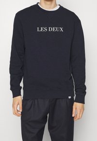 Sudadera azul marino de hombre con la inscripción "LES DEUX" en gris claro. Cuello redondo, puños y dobladillo acanalados, confeccionada con una mezcla de algodón suave.