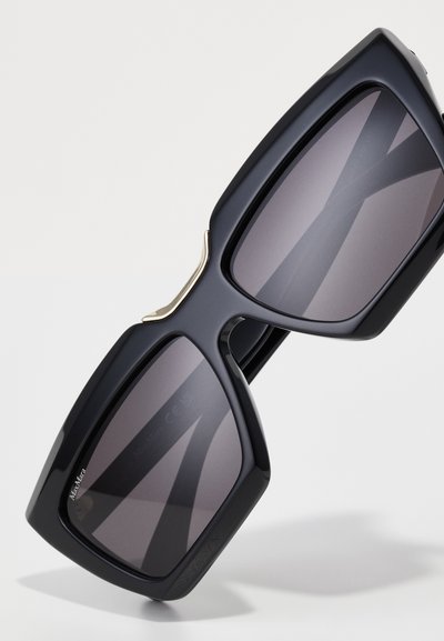 Gafas de sol oversized negras con lentes grises, con un acabado mate, diseño de marco geométrico y un acento dorado en el puente.