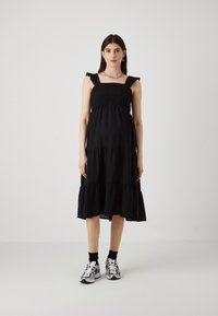 Rochie neagră, cu volane la bretelele umerilor și un corset smockat. Modelul a asortat-o cu adidași albi și șosete negre până la gleznă.