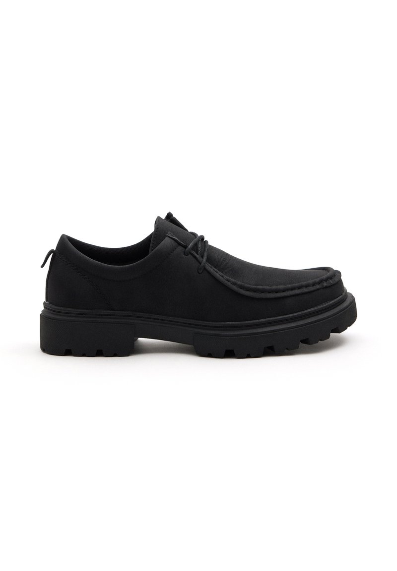 Zapato negro de ante con cordones, punta redondeada, parte superior texturizada y suela de goma resistente. Presenta detalles de costura a lo largo del borde.