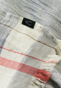 Katoenen schotse sjaal met grijze, witte en rode patronen. Franje-randen en een zwart label met een logo nabij de hoek. Zachte textuur.