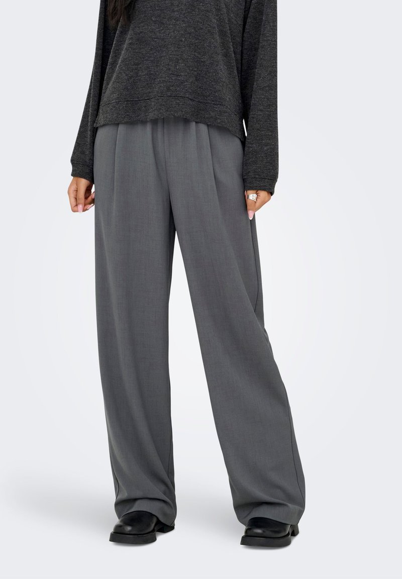 Pantalon à jambes larges en tissu gris clair, présentant une texture lisse et une coupe décontractée. Associé à un haut à manches longues ample et foncé.