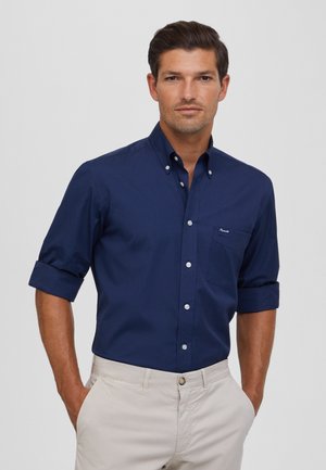 Marineblaues Button-Up-Hemd mit aufgerollten Kurzärmeln, Fronttasche und weißen Knöpfen. Hergestellt aus einem glatten Stoff und mit klassischem Kragen.