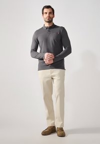 Polo gris de mangas largas con cuello abotonado y bolsillo en el pecho. Combinado con pantalones color crema y mocasines marrones. Textura de tela suave.