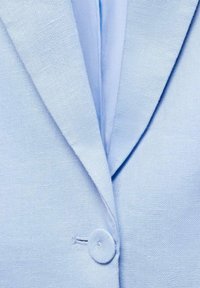 Blazer bleu clair avec col cranté, tissu texturé et fermeture à un seul bouton. Le design est simple et fonctionnel.