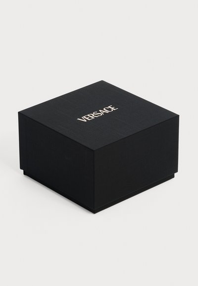 Boîte carrée noire Versace avec surface texturée et logo blanc centré sur le couvercle, sur un fond clair uni.