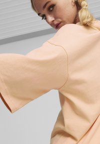 Peachfarvet oversized t-shirt med løse klokkeærmer, lavet af blødt stof. Har et enkelt design og synlige syninger.