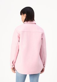 Pink wool-blend shirt jacket with a collar, buttoned cuffs, and a curved hem. Smooth texture, relaxed fit, and visible stitching details.