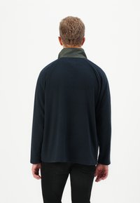 Pullover navy con maniche lunghe e colletto scuro a contrasto. Tessuto morbido e strutturato con una vestibilità rilassata. Indossato con pantaloni neri.