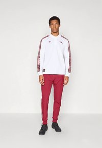 Hvit langermet polo med røde detaljer, kombinert med røde joggebukser med hvite sidestriper. Svarte joggesko fullfører antrekket.