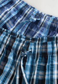 Deux paires de shorts en coton à carreaux bleus avec taille élastique et cordons noués, présentées en gros plan sur fond blanc.