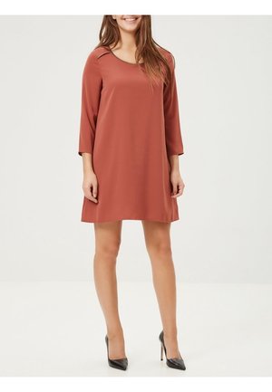 Rostfarbendes, knielanges Kleid mit Dreiviertelärmeln und rundem Ausschnitt, aus glattem Stoff gefertigt, kombiniert mit schwarzen High Heels.