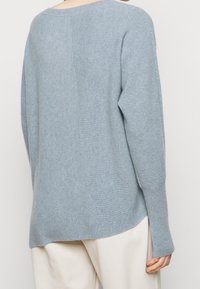 Jasnoniebieski sweter z dzianiny o prążkowanej fakturze, szerokim dekolcie typu łódka i opuszczonych ramionach. Charakteryzuje się luźnym krojem oraz rozcięciami po bokach przy dolnym brzegu.