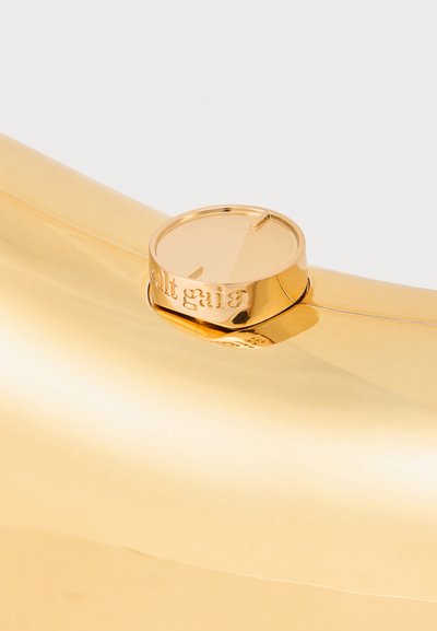 Geantă metalică aurie cu o suprafață netedă și reflectorizantă. Dispune de un închizător circular cu textul "cult gaia". Design elegant și minimalist.