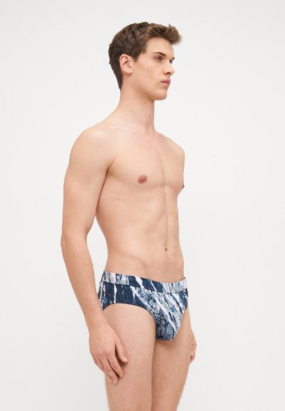 Caleçons de bain avec un motif marbré bleu et blanc, fabriqués en tissu extensible. Dotés d'une taille mi-haute et d'un design ajusté.