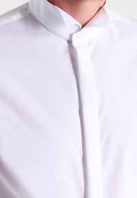 Camicia bianca con bottoni, caratterizzata da una texture morbida, design del colletto classico e un davanti pulito e strutturato con un dettaglio a singolo bottone.