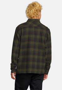 Camisa de franela a cuadros verdes con mangas largas, puños de botón y un corte holgado. Presenta líneas amarillas y rojas que forman un patrón de cuadros.
