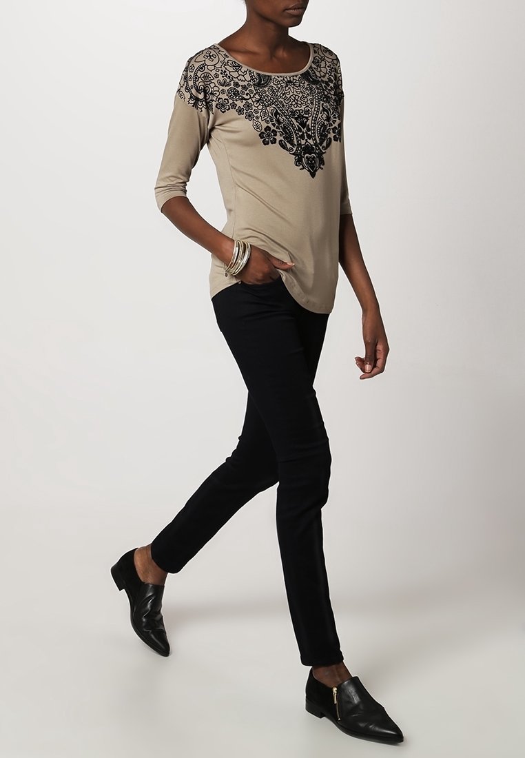 Beige top with black floral embroidery at neckline, three-quarter sleeves, paired with black slim-fit pants and black shoes.