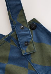 Tissu à motifs bleu et vert avec un design patchwork. Comprend des bretelles réglables et des boutons-pression noirs pour la fermeture. Matière en toile texturée.