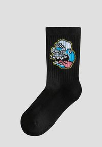 Calcetín de algodón negro con un gráfico colorido y caricaturesco de una cara con un sombrero a cuadros y una lengua grande, con una textura acanalada de fondo.