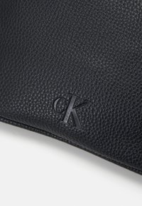 Musta nahkainen käsilaukku, jossa on teksturoitu pinta. Yhdellä sivulla on painettu "ck" -logo. Tyylikäs, suorakaiteen muotoinen.