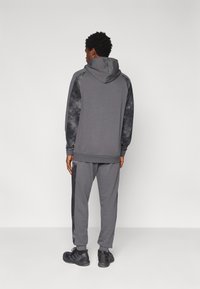 Σετ γκρι φούτερ με κουκούλα και φόρμες με απαλή υφή, με σκούρα μανίκια με σχέδια και πλευρικές ρίγες. Αθλητικά παπούτσια ολοκληρώνουν την εμφάνιση.