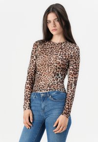 Langsleeve luipaardprint top in bruin en zwart, gemaakt van doorzichtig materiaal met een aansluitend ontwerp, gecombineerd met blauwe jeans.