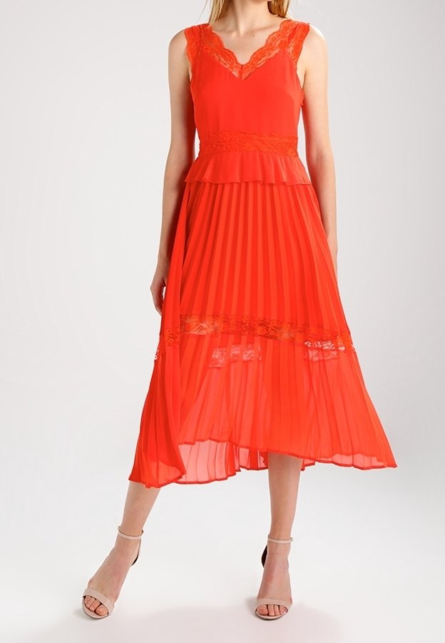 Robe plissée rouge avec détails en dentelle, design sans manches, col en V et ourlet asymétrique. Tissu léger et silhouette en couches.