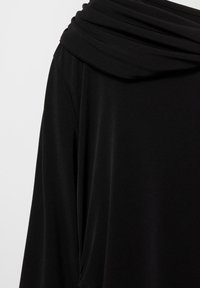 Čierny vrchný diel z tkaniny s drapovaným výstrihom a jemnou textúrou. Dizajn má dlhé rukávy a pohodlný strih.