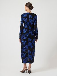 Kvinna som står med ryggen mot kameran iförd en genomskinlig svart klänning med djärva blå blommönster och bruna slingback-hälar.