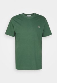 Grön kortärmad t-shirt med rund halsringning och en liten broderad Lacoste-krokodil-logotyp på vänster bröst.