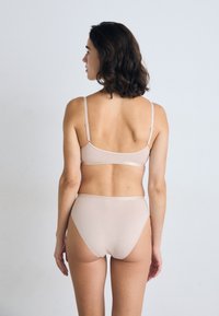 Naakte beha en high-waisted slipset, naadloos ontwerp met dunne bandjes, zachte textuur, minimale hardware en een gladde afwerking.