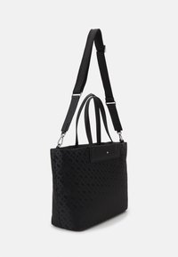 Sac fourre-tout noir en matériau texturé, doté de doubles poignées, d'une sangle amovible et d'une poche avant épurée avec un petit accent.