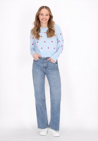 Ljusblå stickad tröja med röda hjärtan, kombinerad med ljusblå raka jeans och vita sneakers.