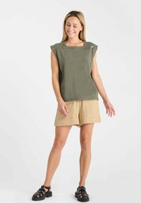 Haut sans manches vert olive avec un décolleté carré et des boutons décoratifs, associé à un short en lin beige et des sandales noires.