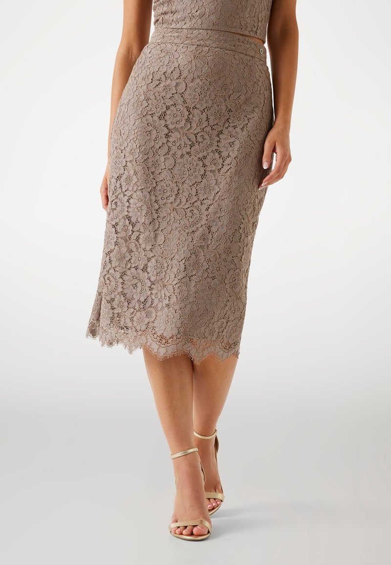 Falda lápiz de encaje en taupe con patrón floral, dobladillo ondulado y un sutil brillo. Combinada con sandalias metálicas de tiras finas.