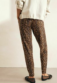 Leopardenmuster-Hosen aus braunem und schwarzem Stoff mit taillierter Passform, kombiniert mit schwarzen Ballerinas. Strukturiertes Muster im gesamten Design.