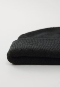 Black knitted beanie, textured fabric, folded cuff section, focuses on ribbed design, soft material, and dark color.