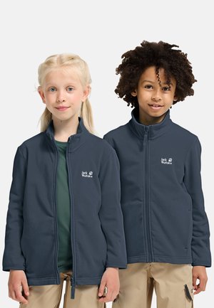 Due bambini indossano giacche in pile blu navy con cerniera e pantaloni beige, in piedi fianco a fianco su uno sfondo semplice.
