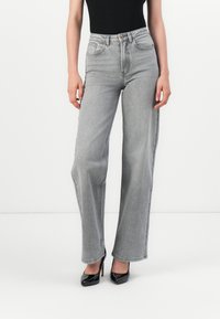Hoge taille grijze denim jeans met een rechte pasvorm, vijf zakken en contrasterende stiksels. Zwarte gepatineerde leren hakken.