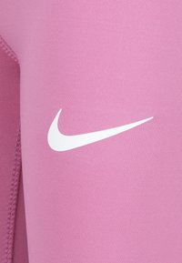 Leggings atletici rosa con una texture liscia, caratterizzati da un logo Nike bianco e dettagli di cucitura lungo il lato, vista ravvicinata.