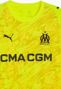 Żółta koszulka sportowa z abstrakcyjnym wzorem, posiadająca okrągły dekolt, czarne loga (Puma i Marsylia) oraz tekst "CMA CGM" wytłuszczony.