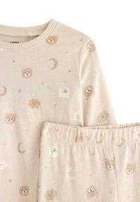 Ensemble de pyjama beige clair comprenant un haut à manches longues et un pantalon, orné de motifs d'ours et de nuages, de lunes et d'étoiles dans des couleurs pastel douces.