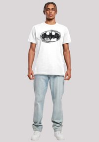 Hvit bomulls t-skjorte med et svart Batman-logo i oval design. Kombinert med lyseblå jeans og hvite joggesko.