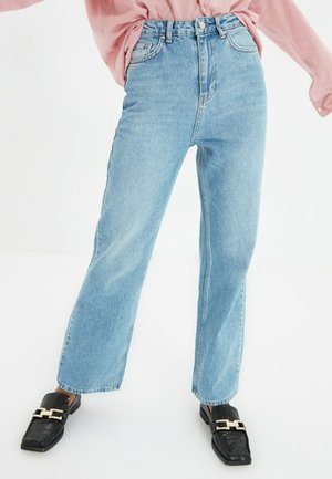 Persona vistiendo unos jeans rectos de cintura alta de color azul claro, mocasines negros con hebilla dorada y una camisa rosa de manga larga metida dentro.