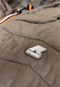 Giacca puffer beige con texture a rombi, dotata di una patch del logo K-Way bianca e di una zip con tirante a strisce multicolore.
