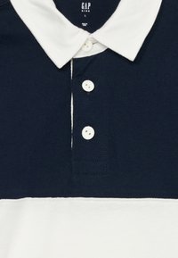 Ναυτικό μπλε και λευκό βαμβακερό πόλο μπλουζάκι με πτυχωτό γιακά, τρεις λευκούς κουμπάκι και σχέδιο οριζόντιων ρίγων.