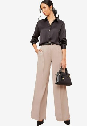 Silk black shirt with button closure, beige wide-leg trousers, black handbag with gold accents, and pointed black heels.