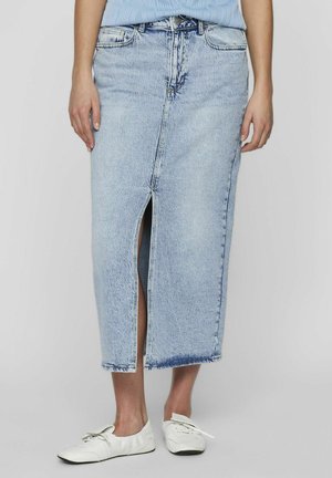 Light blue denim skirt with a front slit, ankle length, and raw hem. Worn with white sneakers, showcasing a casual design.